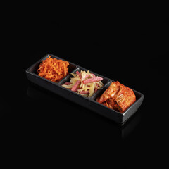 Delicious three section dish featuring vibrant carrot salad, pickled vegetables, and spicy marinated fish, all presented in sleek black tray