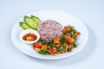 Delicious plate of fried chicken with basil, served with purple rice, cucumber slices, and dipping sauce, showcasing vibrant colors and textures