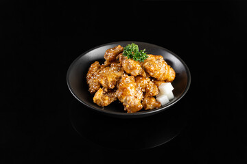 Delicious fried chicken wings coated in savory sauce, garnished with sesame seeds and herbs, served in black bowl. Perfect for food lovers