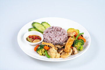 Delicious plate of stir fried vegetables with purple rice, served with dipping sauce and fresh cucumber slices, showcasing vibrant and healthy meal