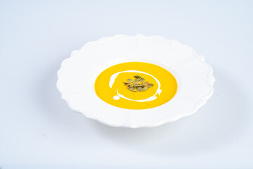 Creamy yellow soup with pumpkin seeds in white plate, showcasing modern culinary presentation