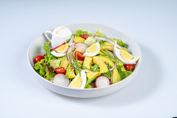Fresh salad with avocado, eggs, cherry tomatoes, and mixed greens, drizzled with dressing, showcasing vibrant colors and healthy ingredients