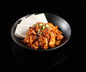 Delicious Asian dish featuring spicy chicken, tofu, and garnishes served in black bowl. vibrant colors and textures create appetizing presentation
