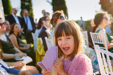 girl in a pink dress is sitting with fan smiling happily