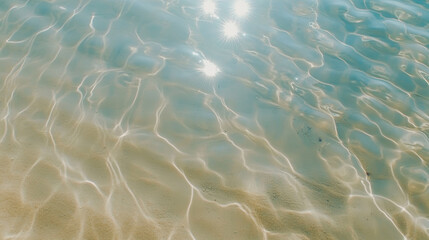 Fototapeta premium Sunlight reflections on clear water with golden ripples over a sandy beach, creating a shimmering pattern and a tranquil summer atmosphere