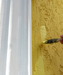 Person is painting a wall with a brush, and the wall is yellow and white