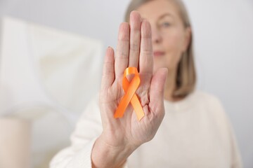 Multiple Sclerosis awareness. Woman with orange ribbon at home, selective focus
