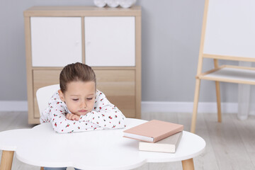Resentful little girl at white table indoors, space for text