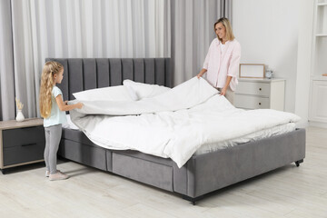 Little girl helping her mother making bed at home