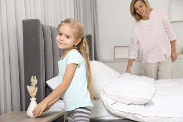 Obraz premium Little girl helping her mother making bed at home