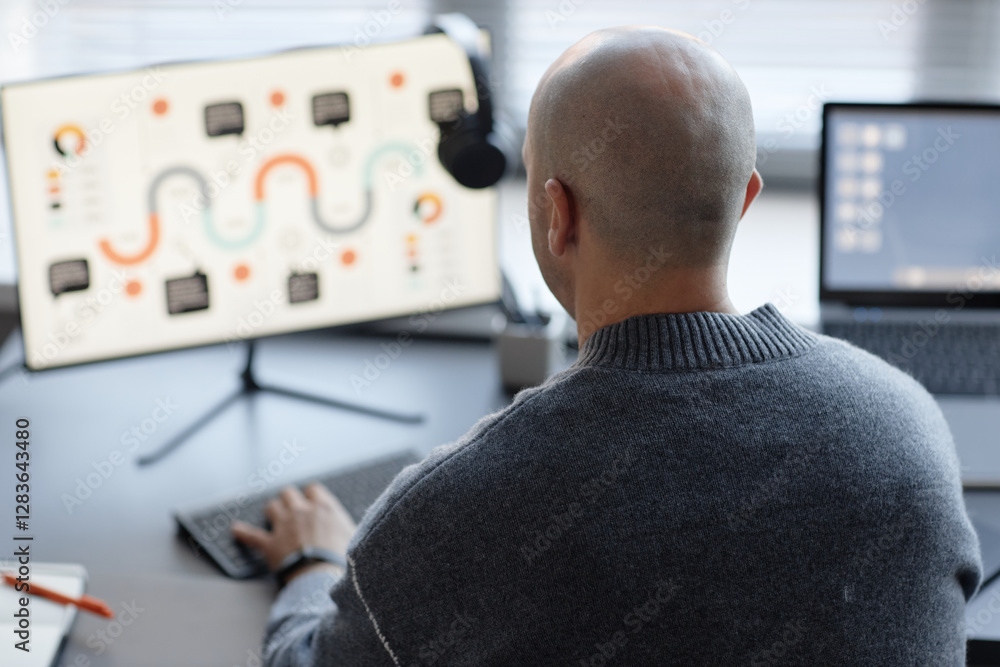 Poster rear view of adult man with shaved head typing on computer keyboard while working in corporate offic
