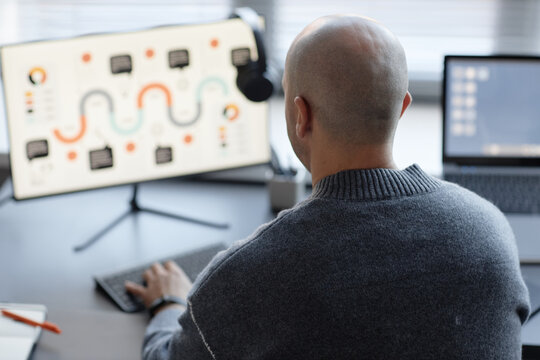 Rear view of adult man with shaved head typing on computer keyboard while working in corporate office - Powered by Adobe