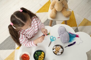Little girl making craft at white table indoors, top view. Child creativity and handmade handicraft