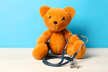 Pediatrics concept. Teddy bear with stethoscope on wooden table against light blue background