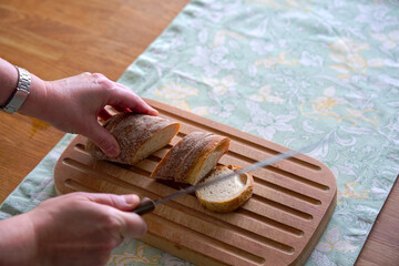 High angle view of wooden breadboard lying on oak table with women hands cutting bread with place...