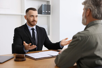 Man having meeting with professional lawyer at wooden desk indoors