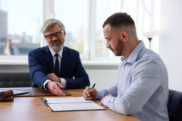 Client signing notarial paperwork during meeting with lawyer at wooden desk indoors, selective focus