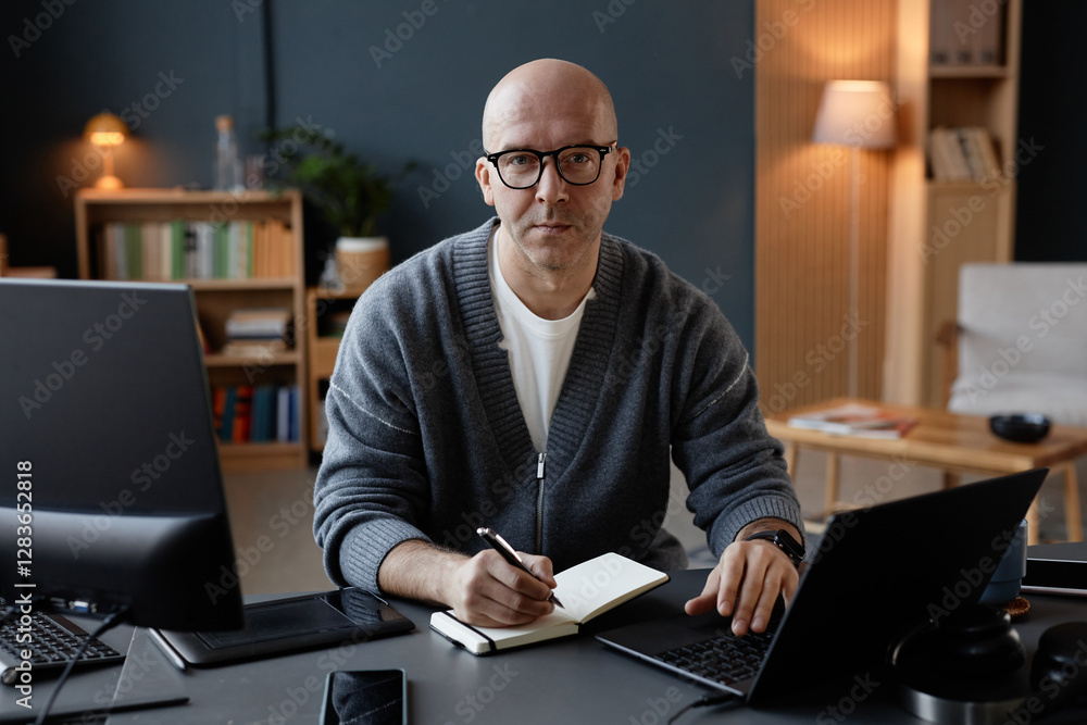 Poster portrait of middle aged man with shaved head looking at camera with calm expression on face, while w