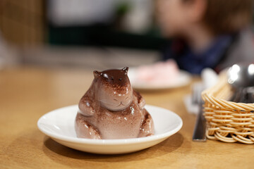 Chocolate  jiggly dessert in shape of capybara on plate in cafe. Dancing jelly animal mousse. Popular korean, japanese pudding.