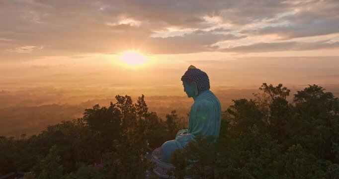 Aerial view of A large Buddha statue stands tall on a mountain.
Aerial hyper lapse view of Beautiful sunrise light at the large Buddha statue on the mountain.