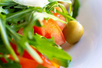 Fresh vegetable salad with tomato and cucumber, olives and arugula and white onion on plate close-up. Proper nutrition. Diet and health. Selective focus, defocus