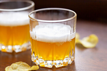 Glass of delicious fresh light unfiltered beer and potato chips on wooden background close up