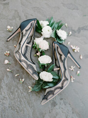 Elegant high heels surrounded by floral arrangements on a textured surface during a styled bridal shoot