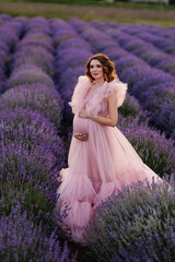 Fototapeta premium a pregnant woman in a pink dress put her hand on her stomach in a lavender field
