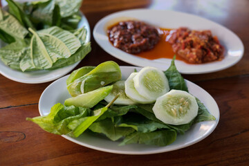 Plates of Indonesian lalapan, featuring fresh vegetables like cucumber and daun pohpohan served...