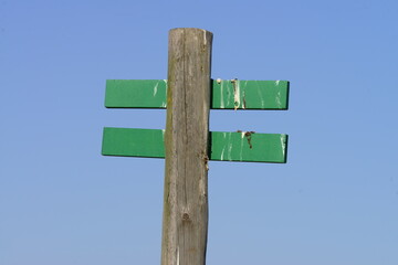 Weathered Wooden Signpost with Blank Green Direction Signs Against Blue Sky