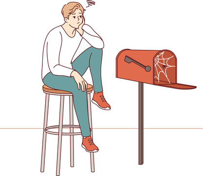 Lonely man waiting for letter, sitting by empty mailbox covered with cobwebs, wanting to receive messages from girlfriend. Lonely guy needs communication and suffers due to lack of friends