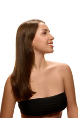 Fototapeta premium Young attractive woman in black top smiling while looking sideways, shows her shining hair against white studio background. Concept of natural beauty, cosmetic products, self-care, wellness.
