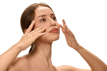 Young, pretty woman massaging face gently with fingertips and gazing upwards against white studio...
