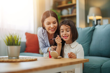 Mother and daughter enjoy a creative moment together while applying makeup at home in a cozy living room setting