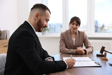 Client signing notarial paperwork during meeting with lawyer at wooden desk indoors, selective focus