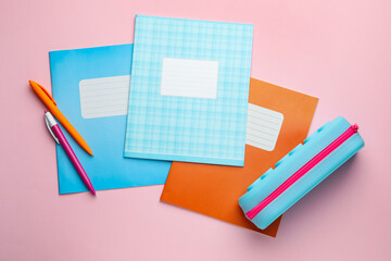 Copybooks, pens and pencil case on pink background, flat lay