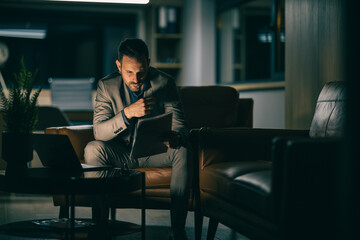 Business professional reviews documents in a dimly lit modern office during late hours