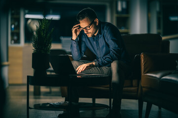 Man working late at night focused on laptop, illuminated by warm light in modern indoor space