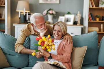Couple shares a joyful moment with flowers in their cozy living room during a sunny afternoon
