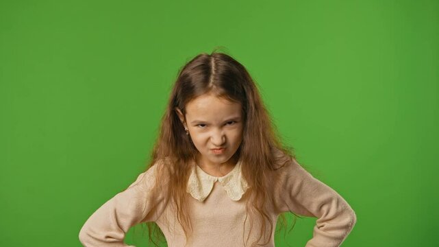 Little girl child with crossed arms and angry face looks at camera, negative expression, isolated on chroma key green screen studio background mockup.
