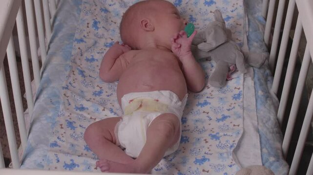 Newborn Infant in Crib Sucking Pacifier
