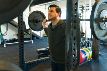 Mid adult man performing a barbell squat in a gym setting, focusing on strength and fitness during...