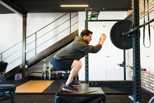 Middle aged chubby man performing box squats in a gym, focusing on strength and fitness training