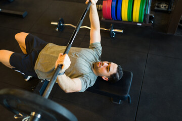 Male athlete performing bench press, gripping barbell intensely, building muscle strength during...