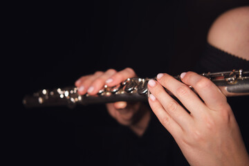 Close-up of musician's hands playing silver flute on a dark background. Studio music photography....
