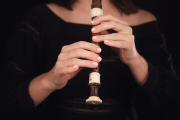 Musician's hands holding and playing a recorder flute on a dark background. Studio music...