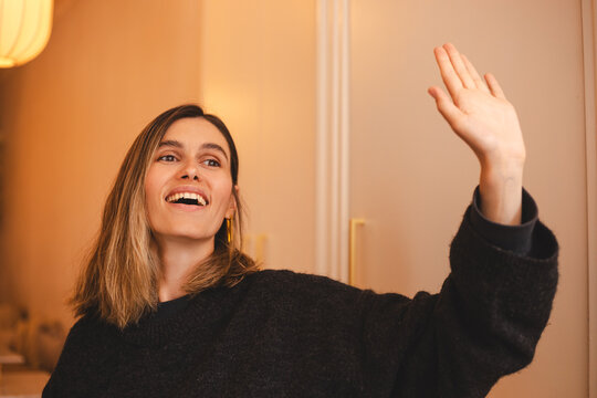Attractive cheerful female make gesture hand wave to say hi hello to her friend walking in cafe restaurant, woman relax casual greeting to her friend in cafe. Woman look happy, wave her hand.