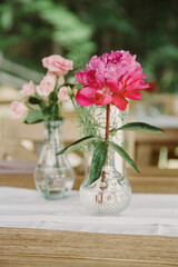 Colorful floral arrangement with pink peony and roses on a wooden table at an outdoor venue during a sunny day