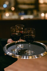 Elegant waitstaff serves three glasses of red wine on a silver tray in a stylish bar setting during the evening