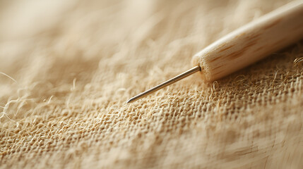 Close-up of a metal needle with a wooden handle resting on a rough-textured fabric surface.